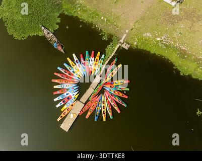 Aus der Vogelperspektive sehen Sie eine lebhafte Auswahl an farbenfrohen Kajaks, die sich um einen kleinen hölzernen Pier gruppieren, der sich in das stille, dunkle Wasser hineinerstreckt, Dhaka, Dhaka Division, B Stockfoto
