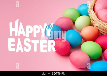 Osterfeier mit bunten Eiern und einem Korb auf rosa Hintergrund Stockfoto