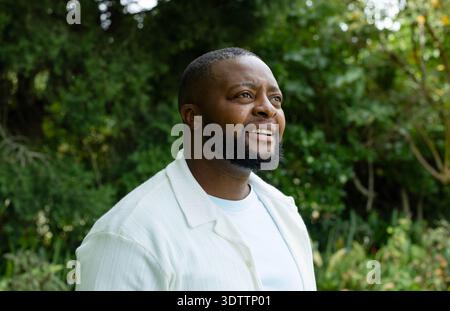 Afroamerikaner, der aufwärts blickt und im Garten lächelt, mit einem weißen T-Shirt Stockfoto