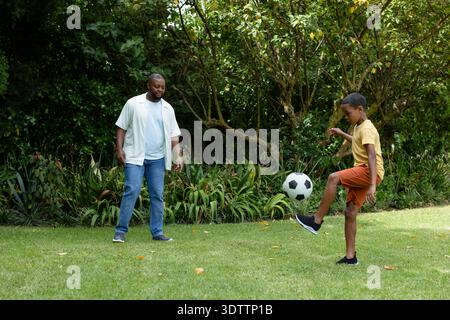 Vater und Sohn spielen mit Fußball im Garten auf Rasen, tragen Turnschuhe und Jeans Stockfoto