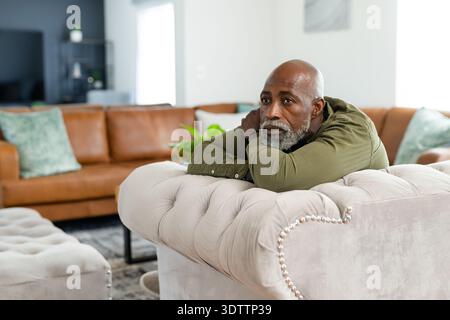 Ranghoher Afroamerikaner, der sich zu Hause auf einem getufteten beigen Sofa stützt, ein olivfarbenes Hemd trägt, einen Kopierraum Stockfoto