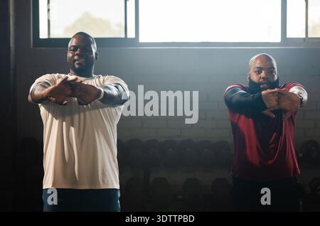 Zwei afroamerikanische Männer in Sportkleidung, die im Fitnessstudio in der Nähe des Hantelständers nach vorne dehnen Stockfoto