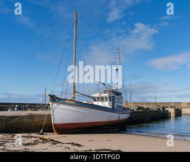 Das Herkules-Boot befindet sich am Sandstrand neben einem Betonpier in Hopeman, Moray, Schottland. Stockfoto