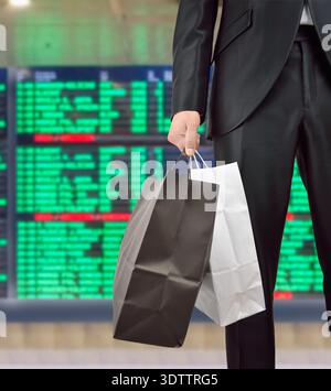 Nahaufnahme eines Mannes mit Einkaufstaschen am internationalen Flughafen mit dem Hintergrund der Fluginformationstafel Stockfoto