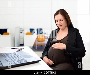 Schuss einer schwangeren Geschäftsfrau, die in ihrem Büro sitzt und ihren Magen und Schmerzen hat Stockfoto