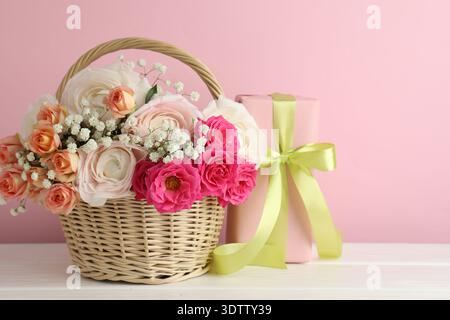Schöne Blumen im Korb und Geschenk auf weißem Holztisch Stockfoto