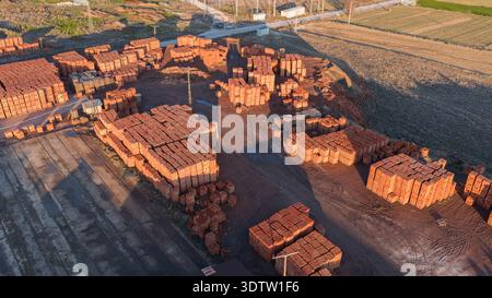 Aus der Vogelperspektive des Lagerbereichs der Ziegelfabrik. Tausende von gestapelten roten Ziegelblöcken und die Industrielogistikstätte im Licht des Sonnenuntergangs. Stockfoto