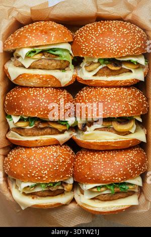 Köstliche hausgemachte Burger mit Rindfleisch- oder Hühnchenkotelett, Käse, Salat und gebratenen Pilzen auf Sesambrötchen aus nächster Nähe. Selektiver Fokus, Draufsicht Stockfoto