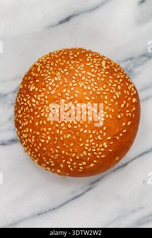 Frisch gebackenes hausgemachtes Sesambrötchen für Hamburger oder Cheeseburger aus nächster Nähe auf Marmorhintergrund. Selektiver Fokus, Draufsicht und Kopierbereich Stockfoto