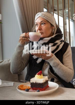 Frau sitzt in einem Café und trinkt Kaffee und genießt einen Dessertkuchen in einem gemütlichen, modernen Café-Shop. Stockfoto