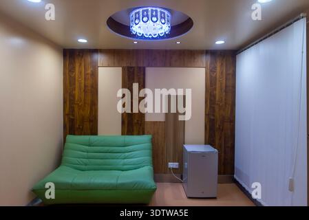 Heller und stilvoller kleiner Wohnbereich mit einem leuchtend grünen Sofa, eleganten Holzwänden und einem leuchtenden Neonschild für eine moderne Spielatmosphäre. Stockfoto