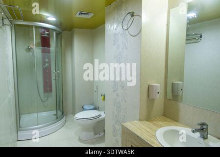 Helles und elegantes, modernes Badezimmer mit Glasdusche, weißer Toilette, Marmorarbeitsfläche und sanfter Beleuchtung für ein sauberes und luxuriöses Ambiente. Stockfoto