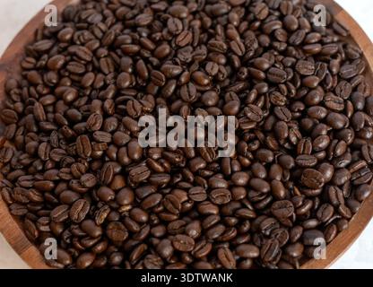 Eine detaillierte Nahaufnahme reichhaltiger, dunkel gerösteter Kaffeebohnen auf einer natürlichen Holzplatte, die Textur und öligen Glanz bei weichem Licht zeigt. Stockfoto