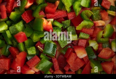 Eine lebendige Nahaufnahme von einer Fülle frisch gewürfelter roter und grüner Paprika, die über die Oberfläche verstreut sind. Die Teile sind unregelmäßig Stockfoto