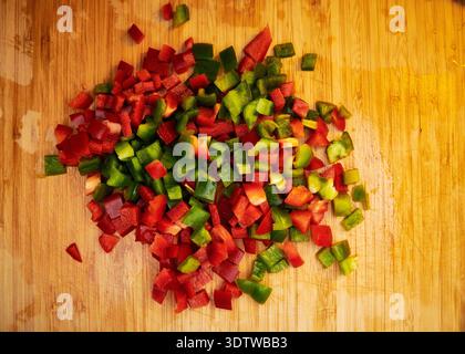 Ein Blick von oben zeigt einen lebhaften Haufen frisch gewürfelter roter und grüner Paprika auf einem warmen Holzschneidebrett. Die Paprika werden klein geschnitten, Stockfoto