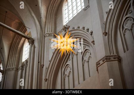 Ein warmes, sternförmiges Ornament, wahrscheinlich ein mährischer Stern, hängt im Inneren einer historischen Kirche oder Kathedrale. Die Architektur fe Stockfoto