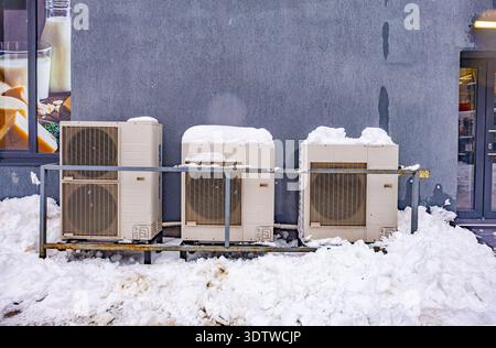 Klimaanlagen im Freien und Wärmepumpen, die nach einem Schneesturm in der Stadt mit Schnee an einer Wand bedeckt sind Stockfoto
