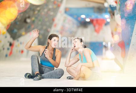 Zwei athletische Frauen sitzen auf dem Boden und diskutieren Möglichkeiten, eine Kletterwand ohne besondere Ausrüstung zu klettern Stockfoto