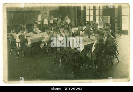 Kinder aus den 1920er Jahren von Kindergarten- oder Grundschulkindern, die an Tischen sitzen und Frühstück, Mittagessen oder Snack essen. Schulkinder der 1920er Jahre um 1925, Großbritannien Stockfoto