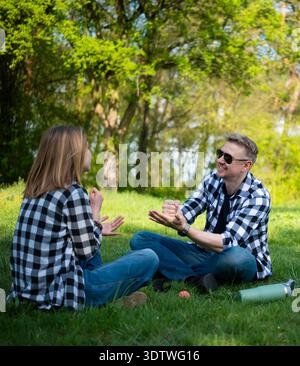 Vater Und Tochter Sitzen Auf Gras Im Summer Park Und Spielen Steinpapier-Schere Stockfoto