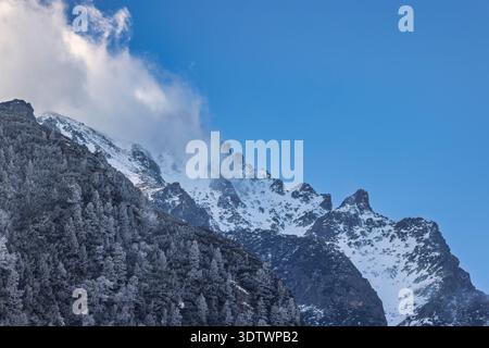 Malerische Landschaft mit einem schneebedeckten Berg, der teilweise von Wolken bedeckt ist, mit einem dichten Wald, der die unteren Hänge bedeckt, unter einem klaren blauen Himmel Stockfoto