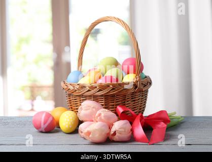 Ostereier im Korb und Tulpenstrauß auf dem Tisch vor verschwommenem Fenster. Leerzeichen für Text Stockfoto