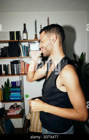 Seitenansicht eines lächelnden jungen Mannes, der zu Hause durch eine alte Videokamera filmt Stockfoto