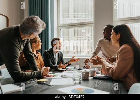 Ein Team aus lächelnden Geschäftsleuten diskutiert Ideen, während sie im Besprechungsraum um den Tisch sitzen Stockfoto