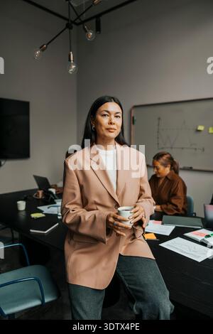 Porträt einer selbstbewussten Geschäftsfrau, die eine Kaffeetasse hält, während sie im Besprechungsraum posiert Stockfoto