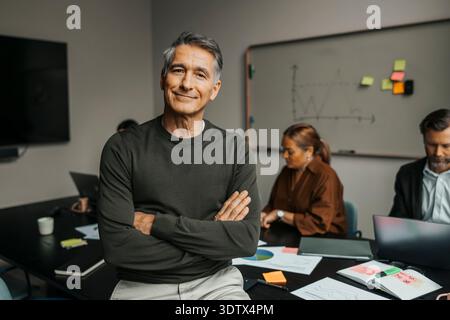 Porträt eines lächelnden Geschäftsmannes, der mit überkreuzten Armen im Besprechungsraum posiert Stockfoto