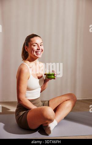 Porträt einer lächelnden Frau, die zu Hause auf der Trainingsmatte sitzt Stockfoto