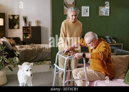 Ältere kaukasische Frau hilft älteren Männern beim Stehen mit Walker-Gerät Stockfoto