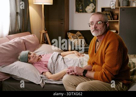Senior kaukasischer Mann tröstet kranke ältere kaukasische Frau, die im Bett ruht Stockfoto