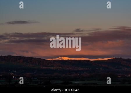Blick auf einen weit entfernten, schneebedeckten Berggipfel, der unter einem rosa Sonnenaufgangshimmel leuchtet Stockfoto