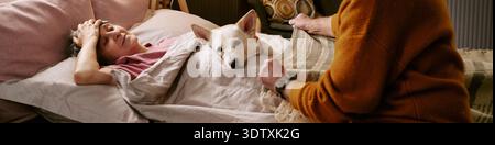 Ältere kaukasische Frau liegend im Bett mit Hund, während sich der Mann kümmert Stockfoto