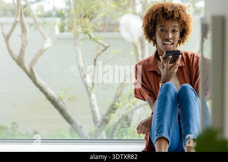 Afroamerikanerin sitzt auf breitem Schweller und spricht in Rosthemd ins Telefon, beobachten, Kopierraum Stockfoto