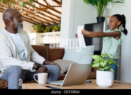 Afroamerikaner Senior Mann und Mädchen sitzen auf dem Sofa und beobachten den abgestuften Papierkopf A, Kopierraum Stockfoto