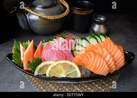 Eine Auswahl an Sashimi-Platten mit frischem Lachs, Thunfisch und Krabbenstangen, elegant mit Gurkenscheiben und Zitronenscheiben, serviert auf Eis. Stockfoto
