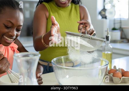 Afroamerikanerin und Jugendfrau sieben Mehl durch Sieb in Schüssel, während sie Eier rührend Stockfoto