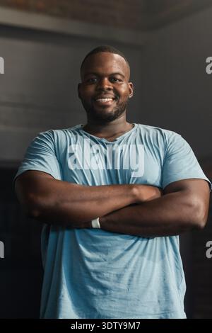 Afroamerikaner, der in schwach beleuchtetem Studio steht, trägt ein hellblaues T-Shirt und ein weißes Armband Stockfoto
