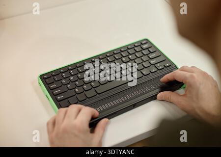 Junger erwachsener Mann mit Braille-Tastatur in Bibliothekseinstellung Stockfoto