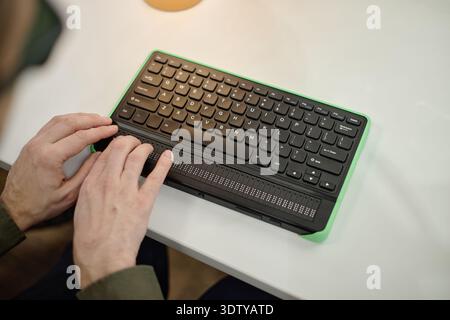 Junger erwachsener Mann mit Braille-Tastatur beim Lesen in der Bibliothek Stockfoto