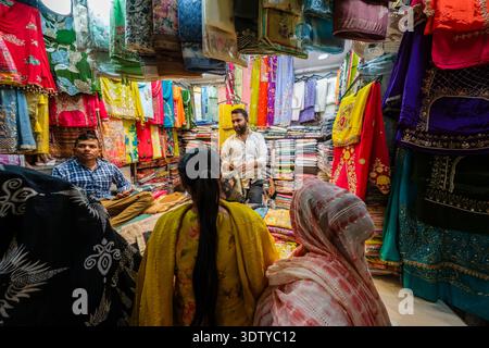 Kunden, die bunte Stoffe und traditionelle Kleidung in einem kleinen Geschäft im Kinari Bazar, Alt-Delhi, suchen. Verkäufer sind in der Entfernung sichtbar. Stockfoto