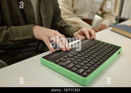 Junger Mann, der Braille-Tastatur benutzt, während er Buch in der Bibliothek liest Stockfoto