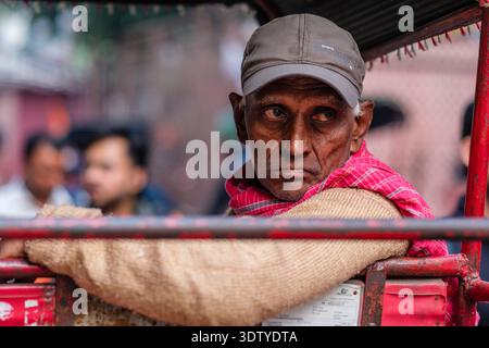 Ein Rikscha-Fahrer mit Mütze hält Ausschau nach Kunden, während er auf der geschäftigen Chandni Chowk-Durchgangsstraße in Alt-Delhi wartet. Stockfoto