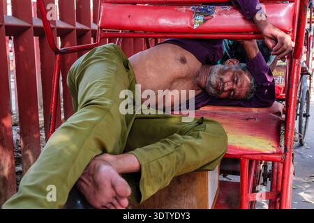 Ein Rikscha-Fahrer schläft ruhig über die roten Sitze seines Fahrzeugs, der entlang der geschäftigen Chandni Chowk-Durchgangsstraße in Alt-Delhi parkt. Stockfoto
