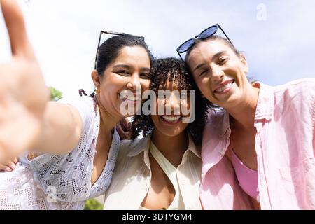 Verschiedene Freundinnen posieren für Selfie im Park mit einer Sonnenbrille, die Telefon und Lichtschichten hält Stockfoto