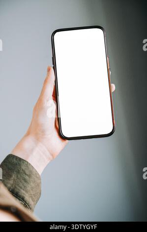 Nahaufnahme einer Hand, die ein modernes Smartphone mit einem leeren weißen Bildschirm hält, ideal für Mockups von Apps, Websites oder mobilen Schnittstellen. Saubere, minimalistische Komposition Stockfoto