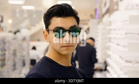 Junger, stilvoller Mann, der Luxussonnenbrillen im Optikgeschäft anprobiert Stockfoto