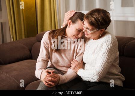 Ältere Mutter Konsolen, tröstende traurige Erwachsene Tochter, die zu Hause auf dem Sofa sitzt. Support in zwei Altersgenerationen || Modell veröffentlicht Stockfoto